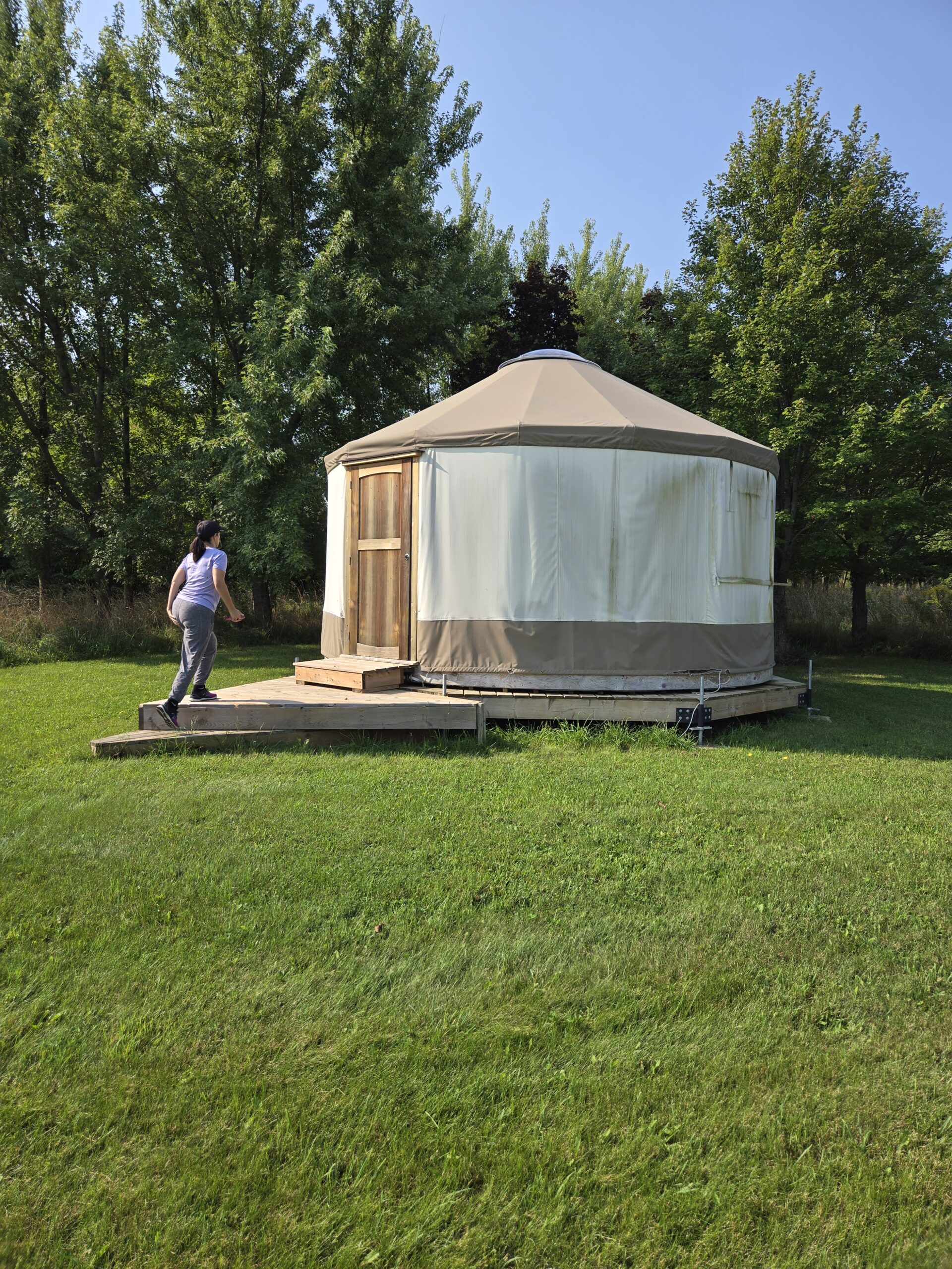 Woman stepping onto deck of canvas yurt on green farm lawn