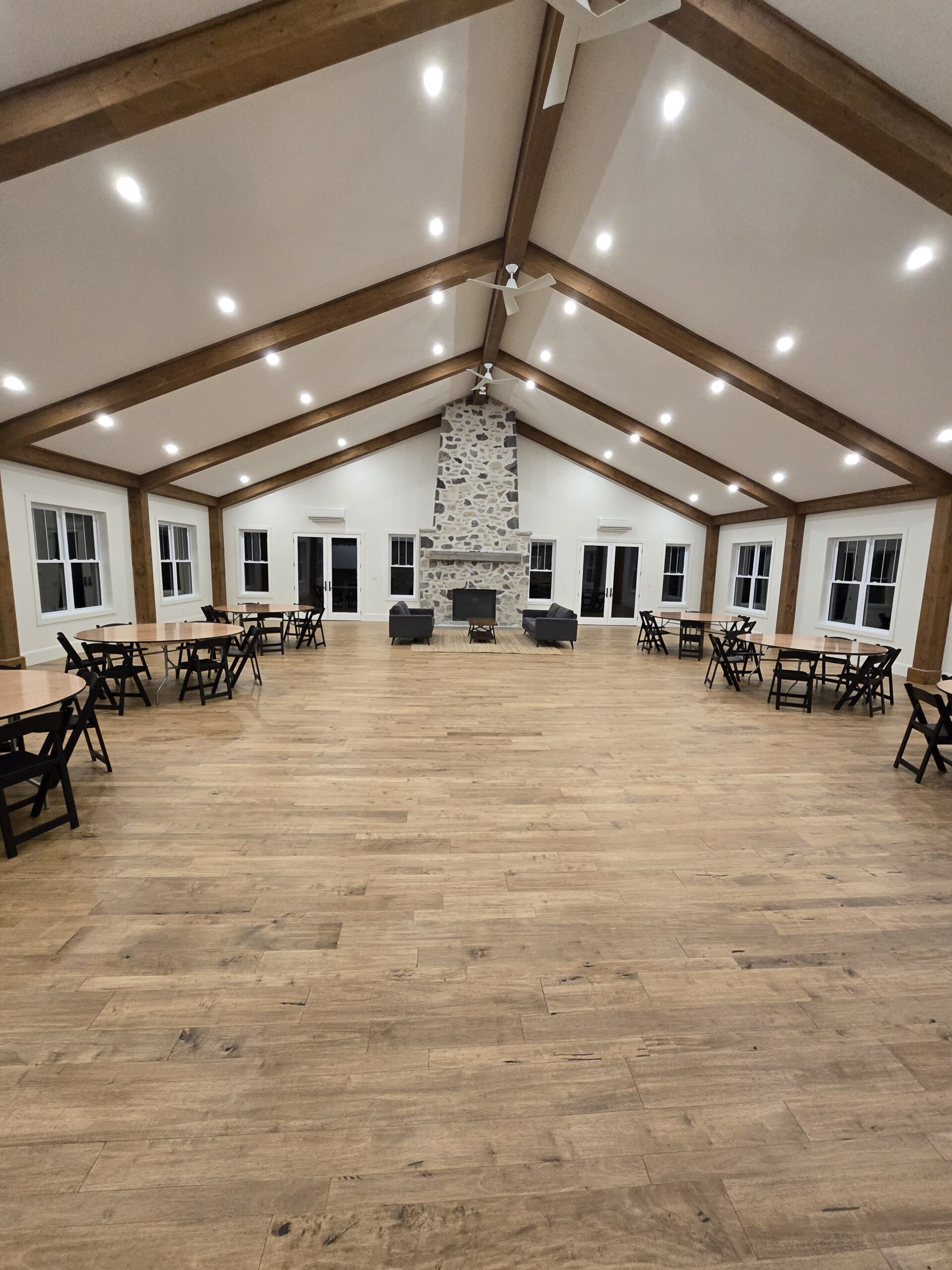 Spacious event hall with vaulted wood-beam ceiling, stone fireplace and round tables
