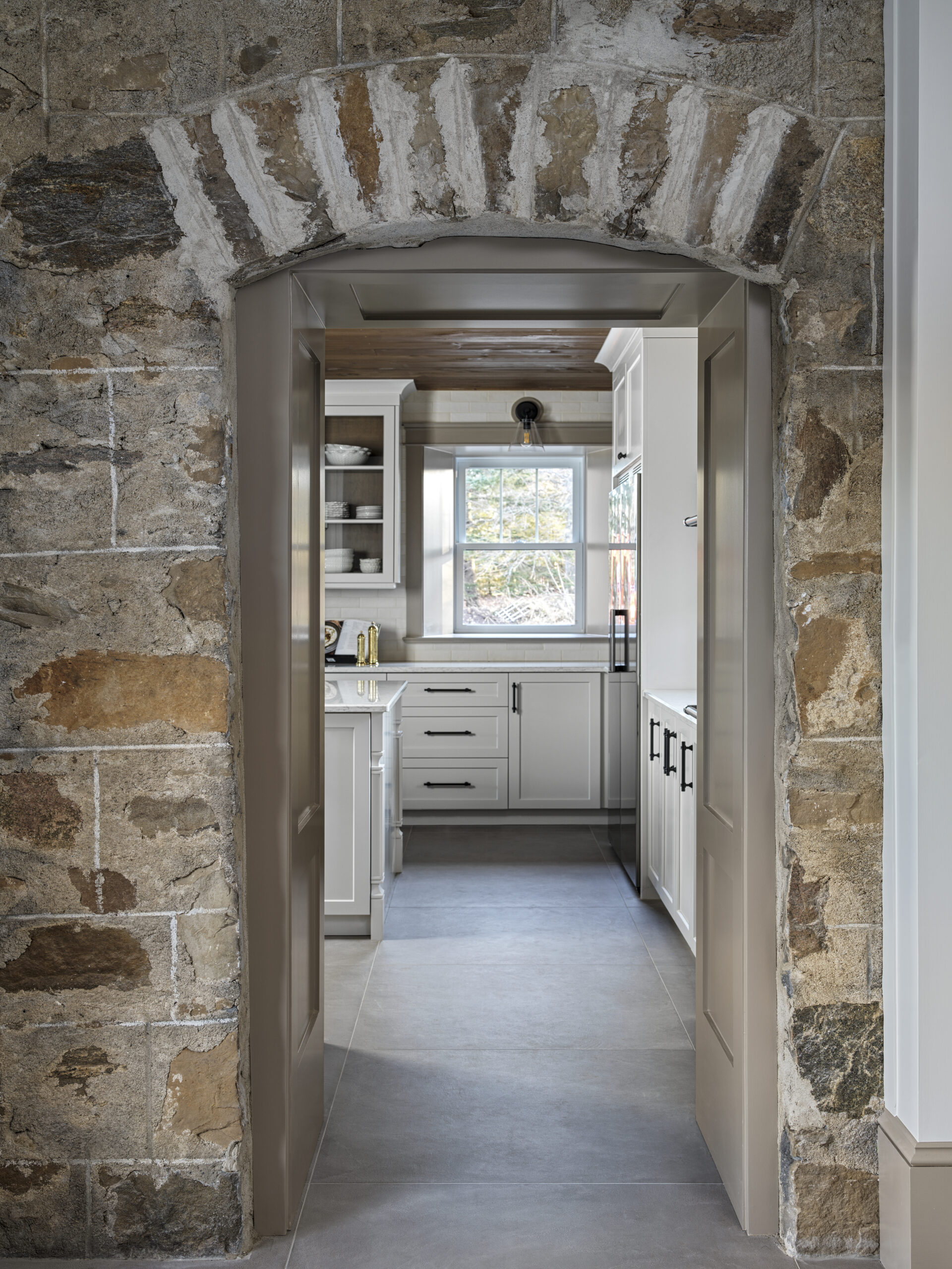 Stone archway opening into a bright white farmhouse kitchen
