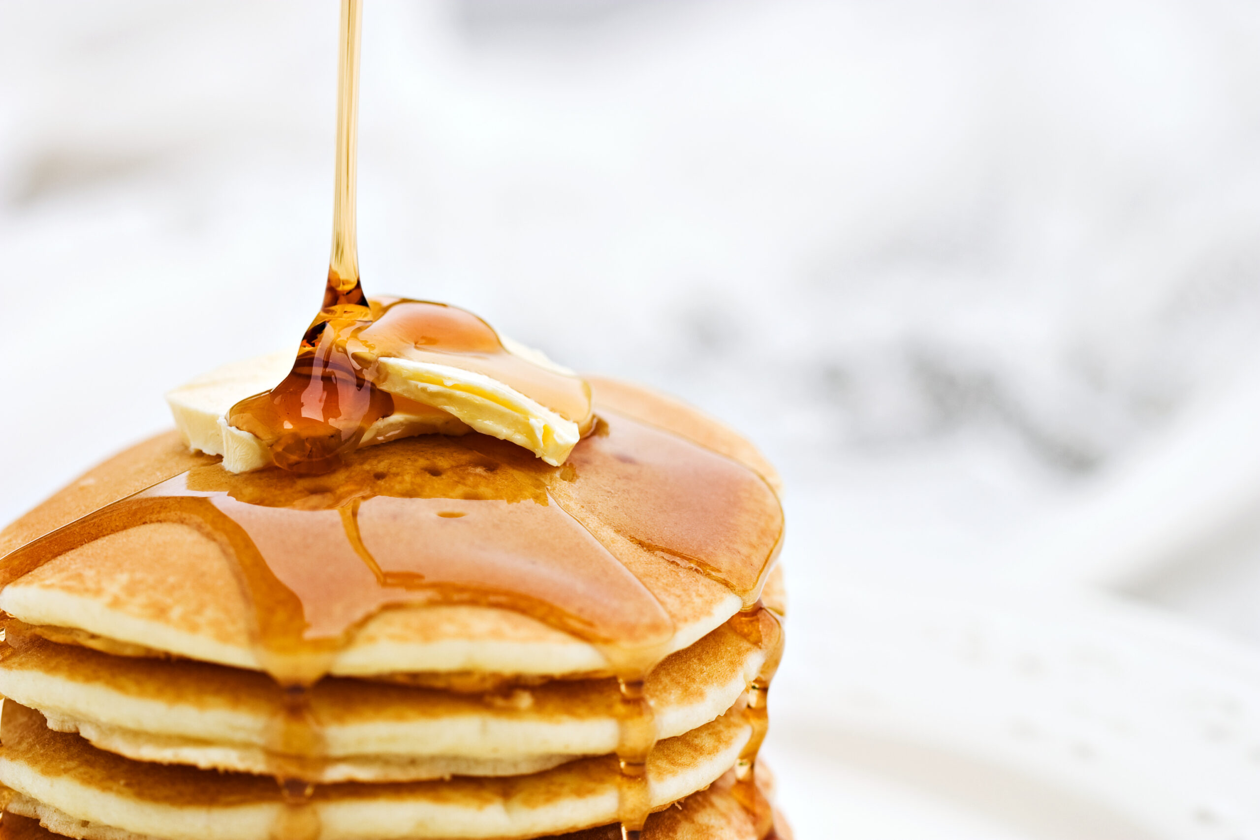 Maple syrup poured over a stack of buttered pancakes