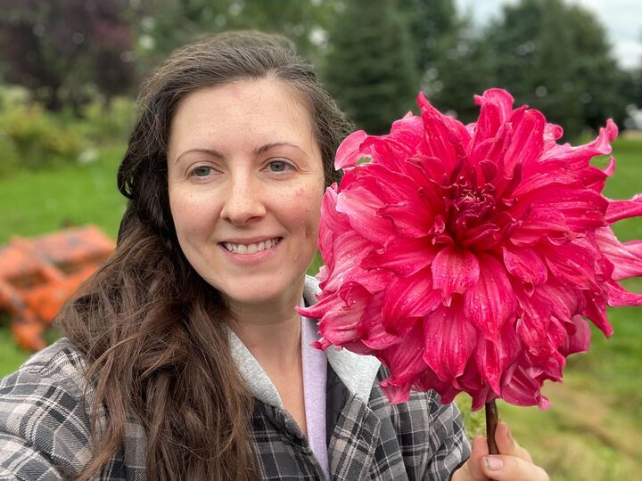 Woman smiling while holding a large pink dahlia bloom outdoors
