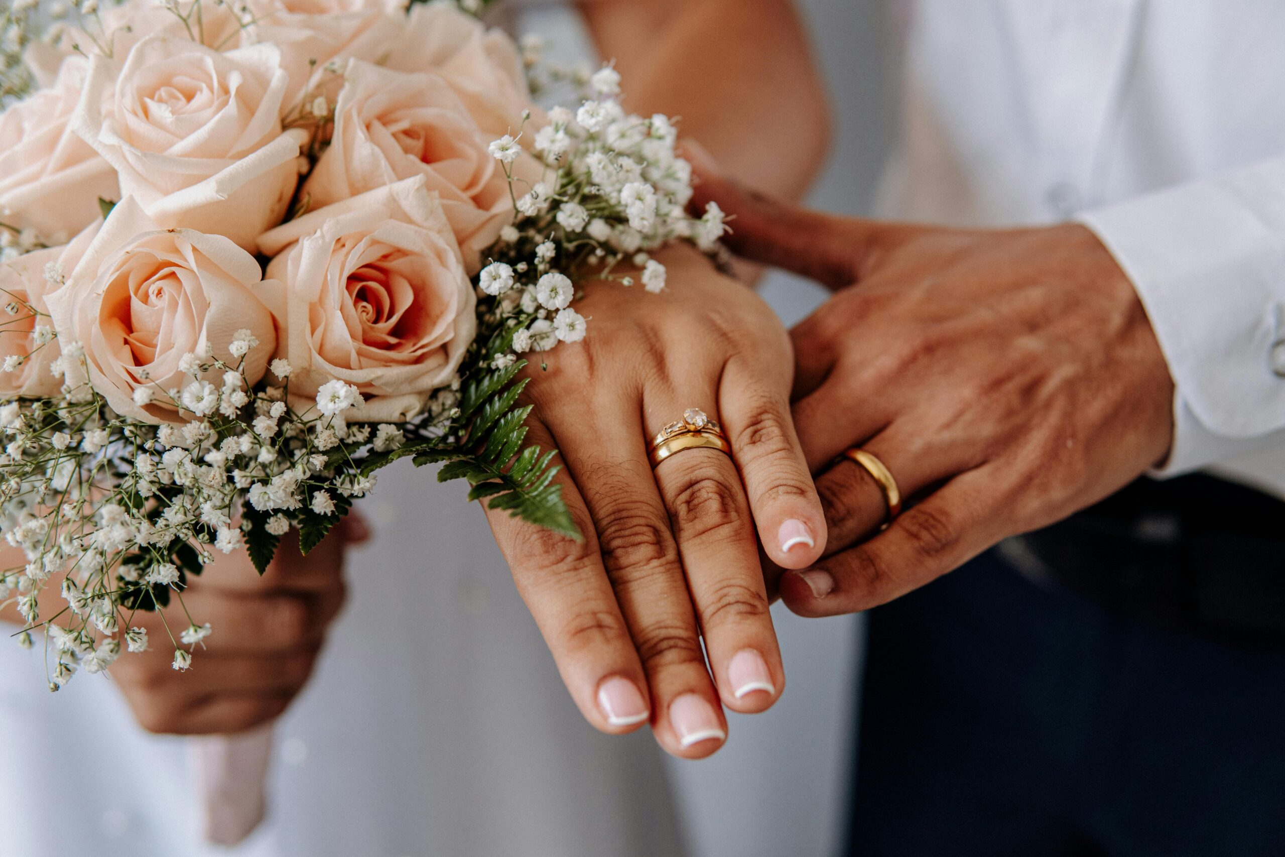 Newlywed couple's hands with wedding rings resting on a blush rose bouquet